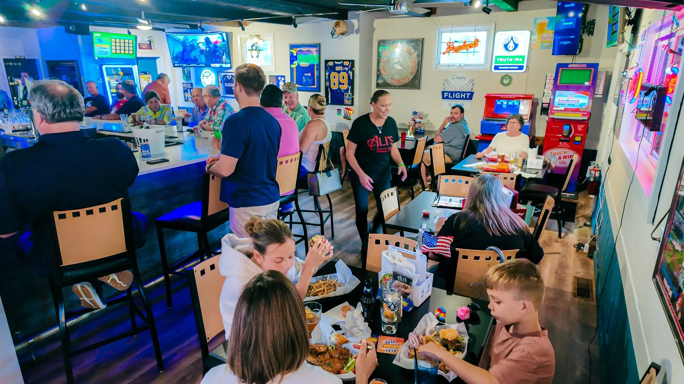 A busy evening in the bar room: families and friends eating at the tables and the bar, with TVs, sports memorabilia and neon on the walls