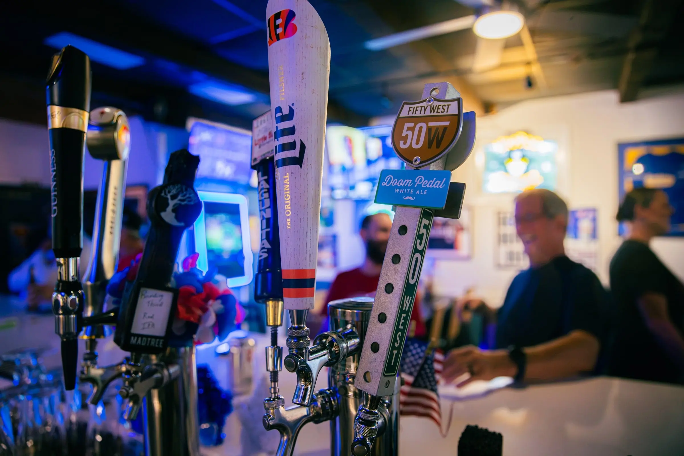 Draft beer tap handles at the bar in blue light, with regulars blurred in the background