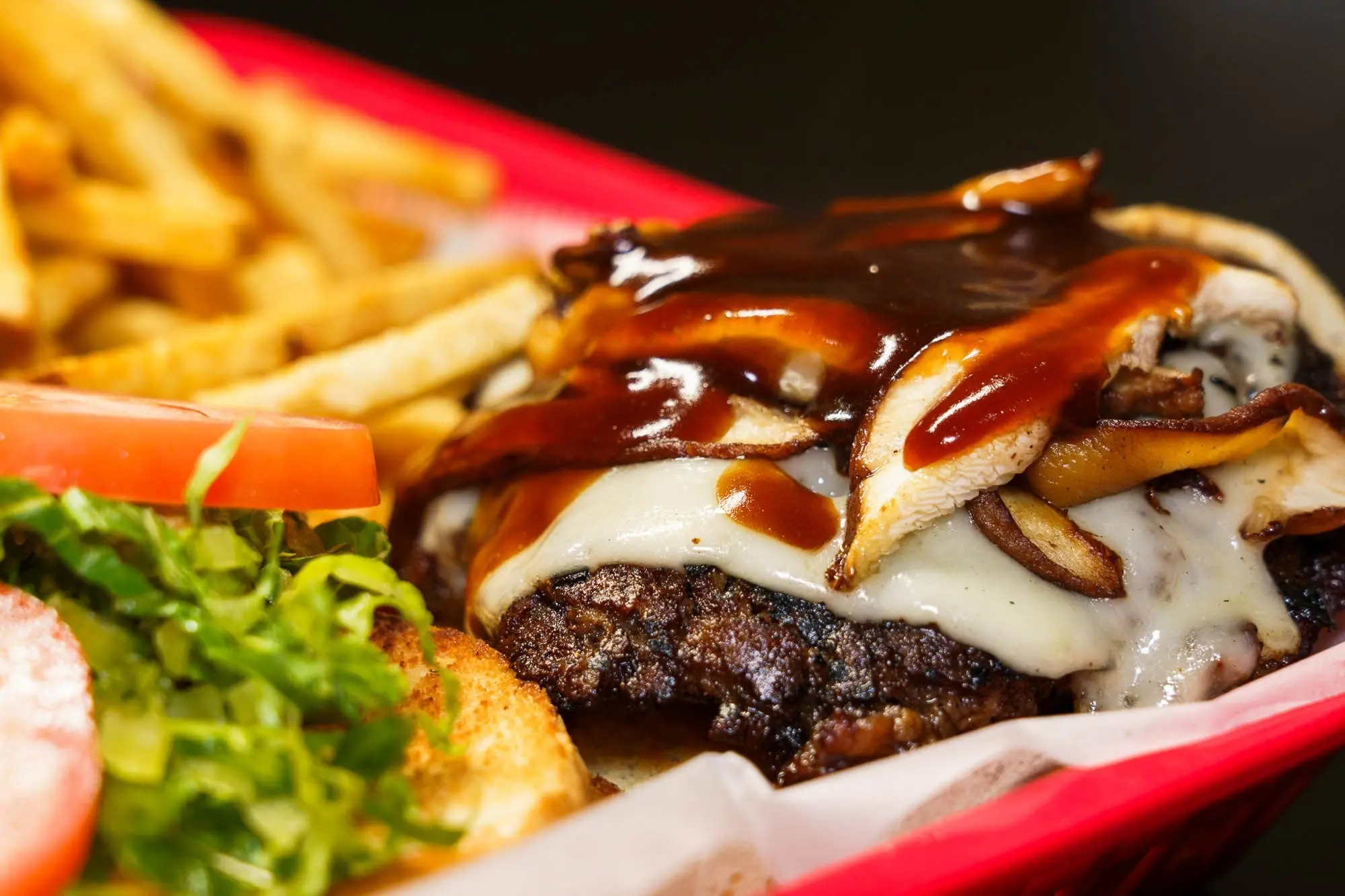 Mushroom Swiss burger with a glossy sauce, lettuce and tomato in a red basket with fries