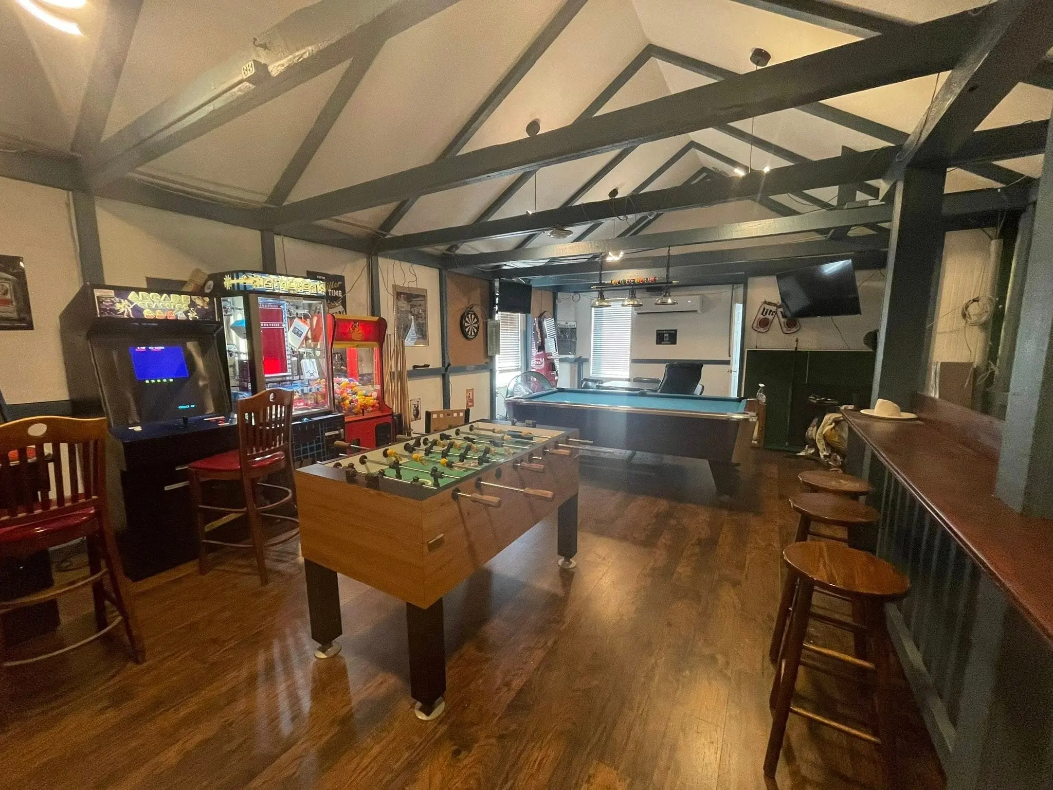 The game room under exposed beams: a foosball table, a pool table, arcade cabinets and a claw machine