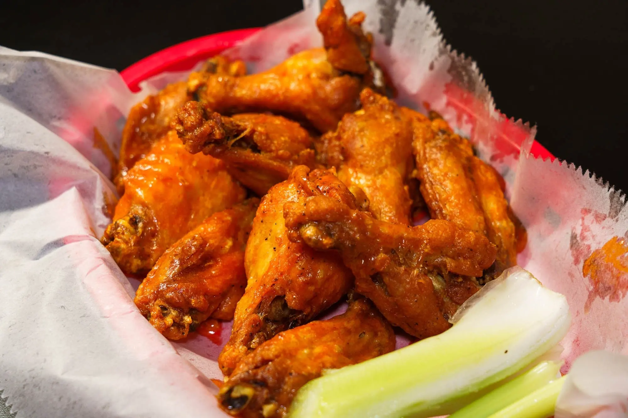 A red basket of saucy jumbo chicken wings with celery sticks