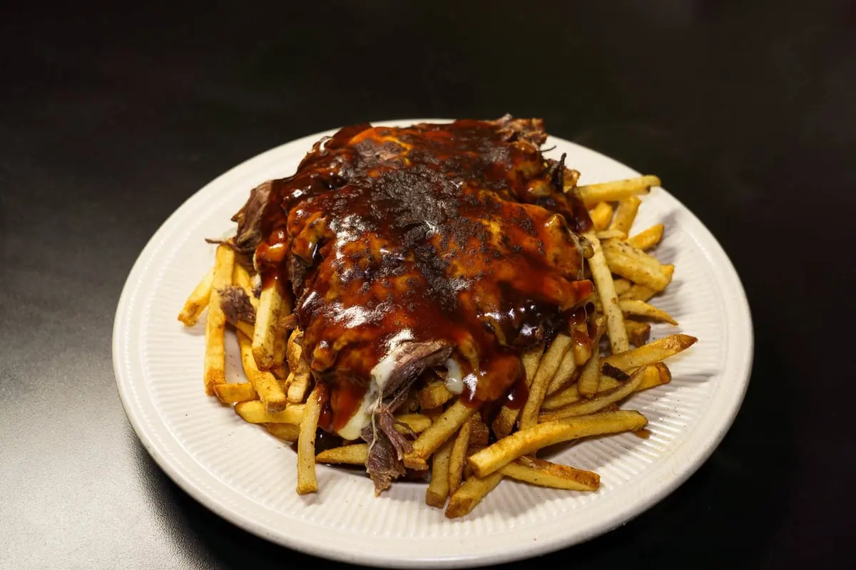 Truffled short-rib poutine: hand-cut fries under braised short rib, cheese curds and demi-glace on a white plate, on a dark table